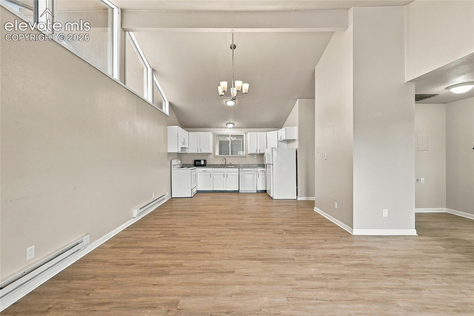 Vaulted ceilings with clerestory windows, wood-finish flooring, and a kitchen featuring white cabinetry and stone-look countertops