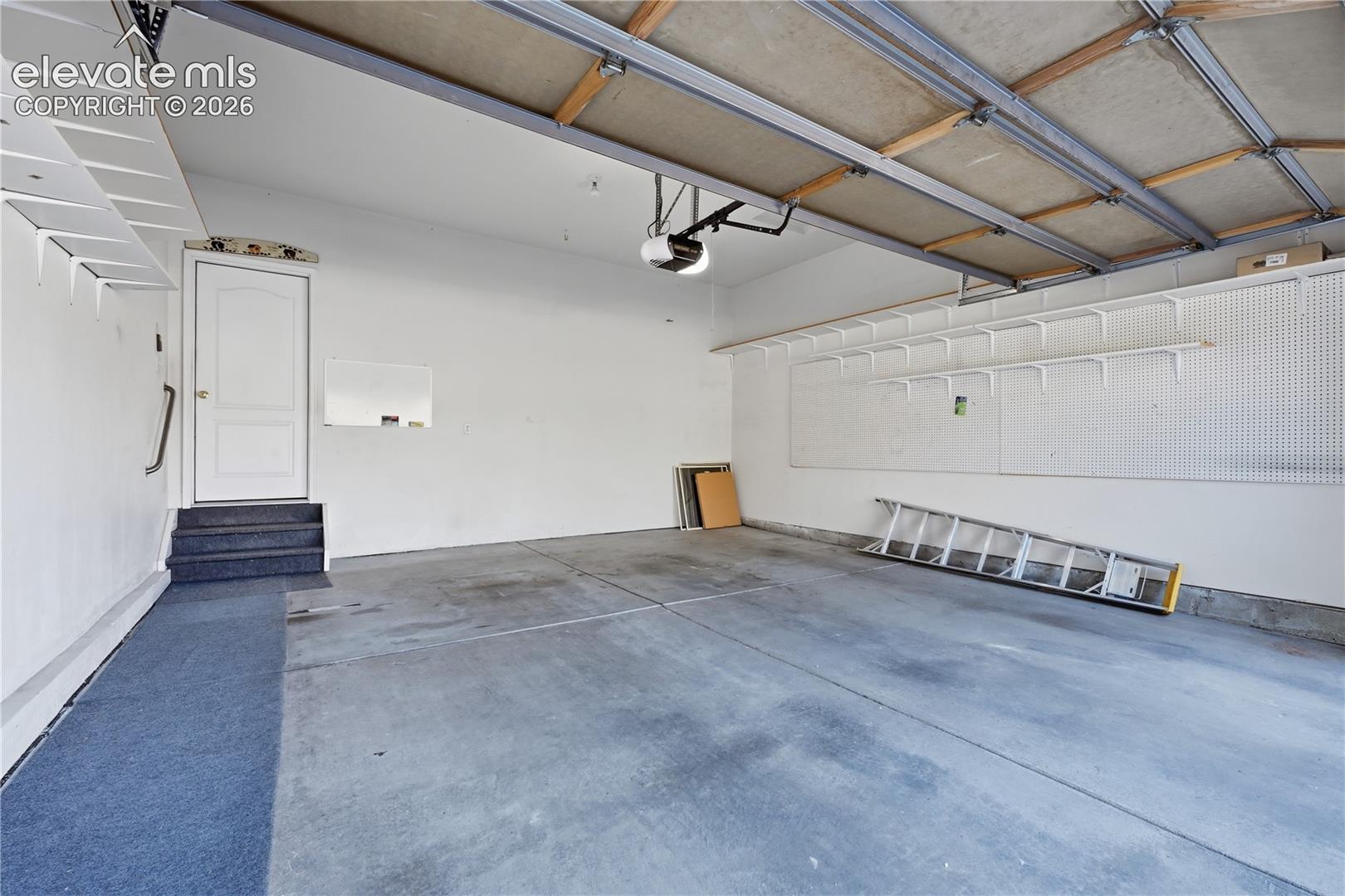 Two-car garage featuring a concrete floor, built-in wall shelving, pegboard organizational paneling, and an interior access door with a step entry