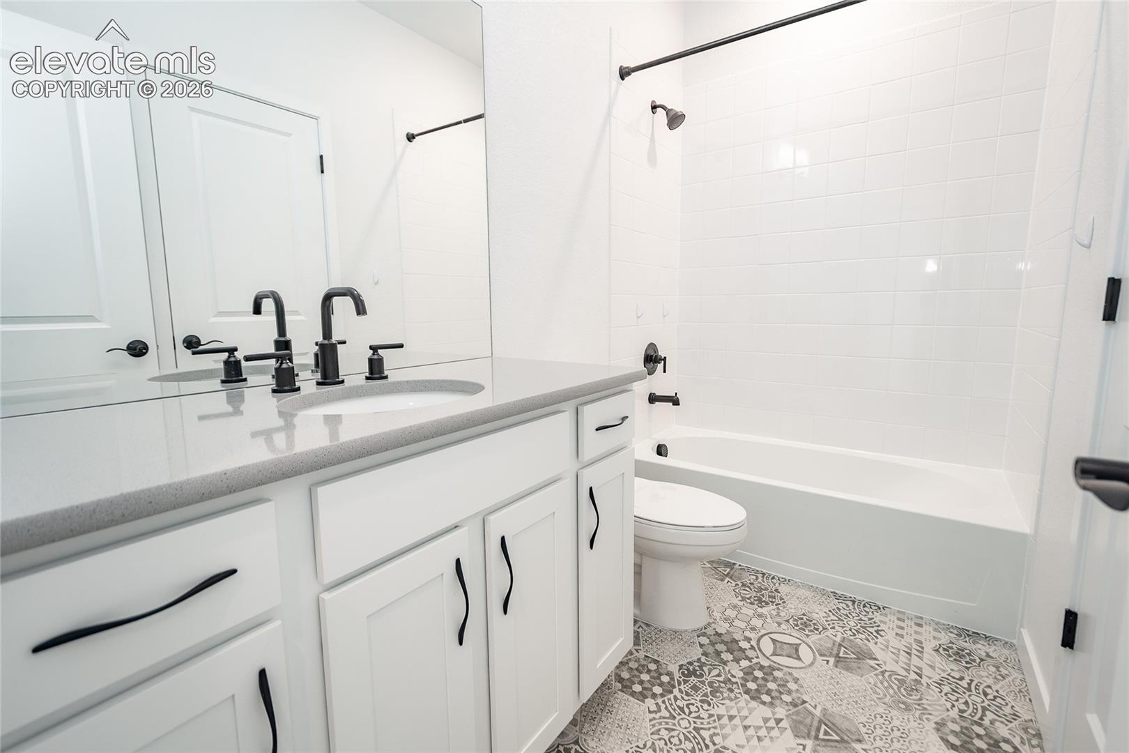 Bathroom featuring a white vanity with a solid-surface countertop, an undermount sink, patterned tile flooring, and matte black hardware