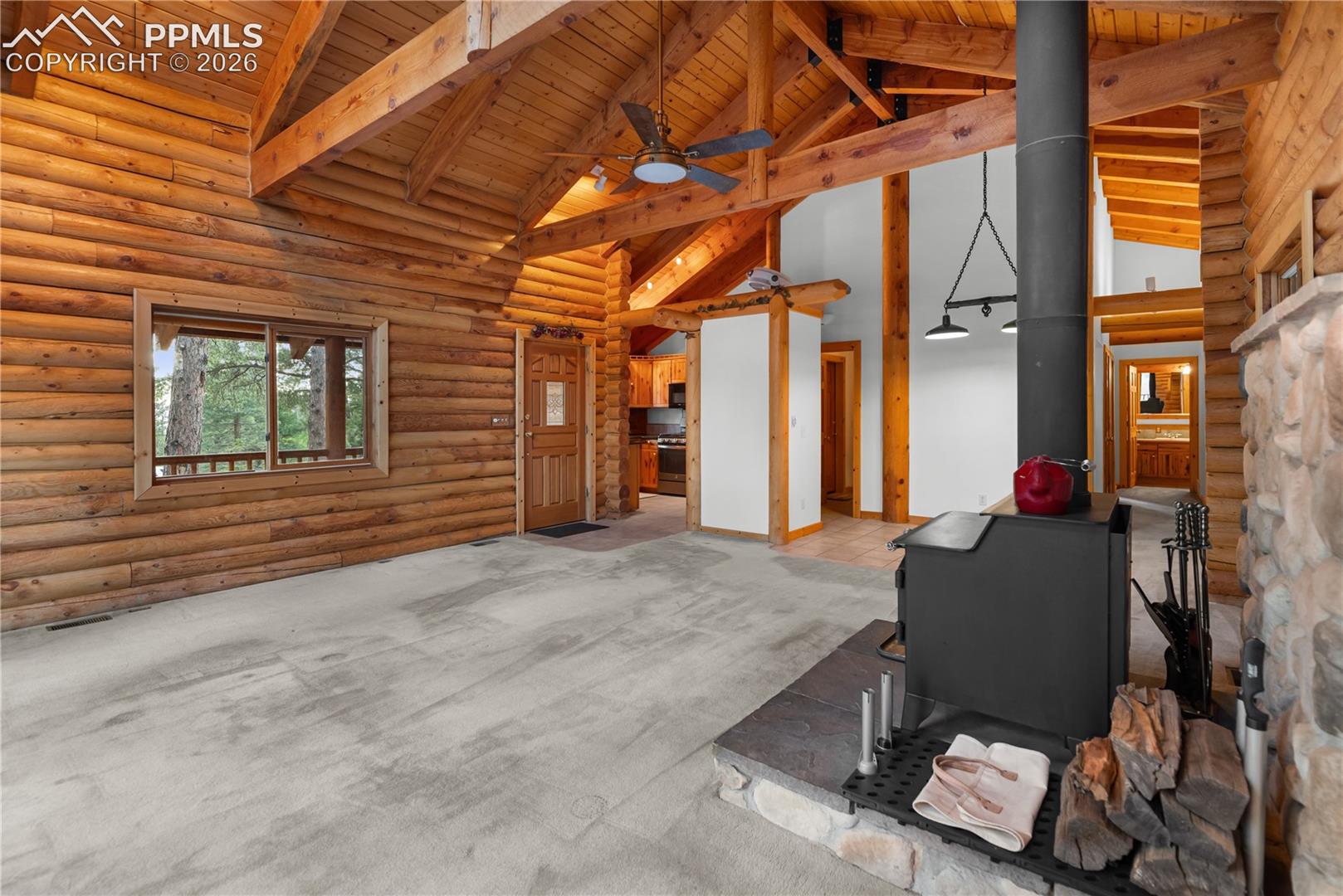 Living room with a wood stove, high vaulted ceiling, ceiling fan, a wooden ceiling with exposed beams, and carpet flooring