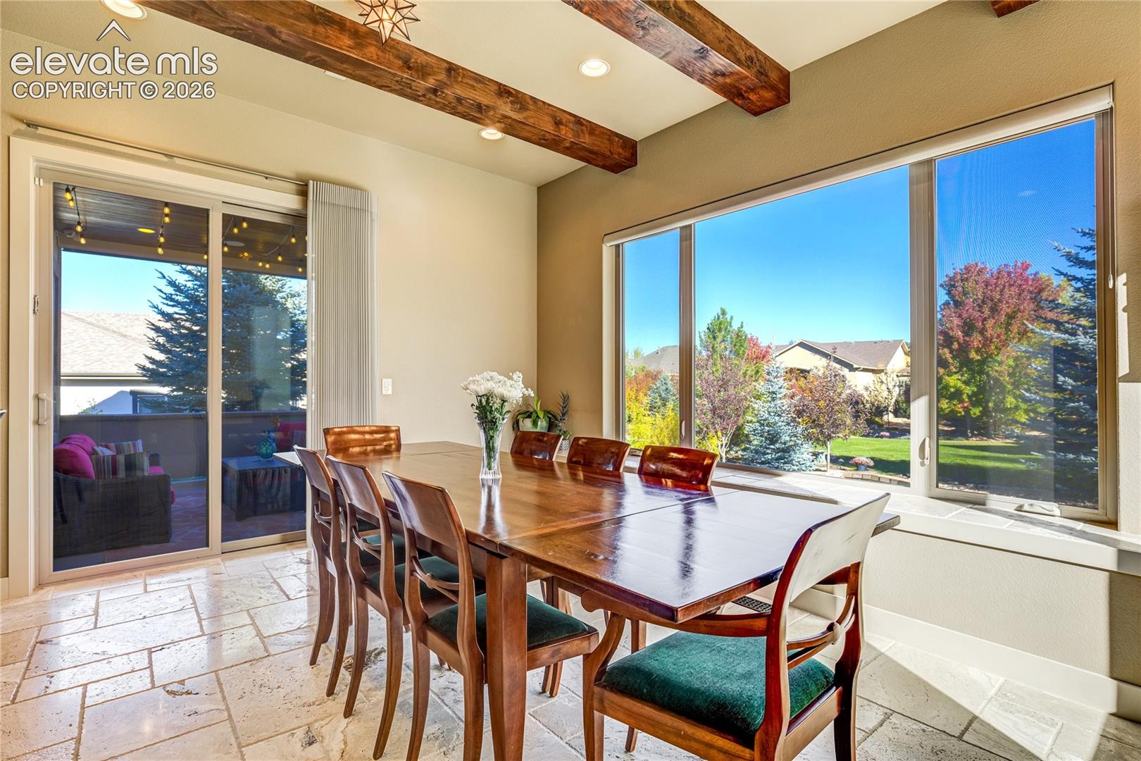Expansive windows frame the colorful landscaping, while direct access to the covered patio connects indoor dining with Colorado's outdoor lifestyle. Stained ceiling beams + travertine flooring lend timeless character to this sun-filled space.