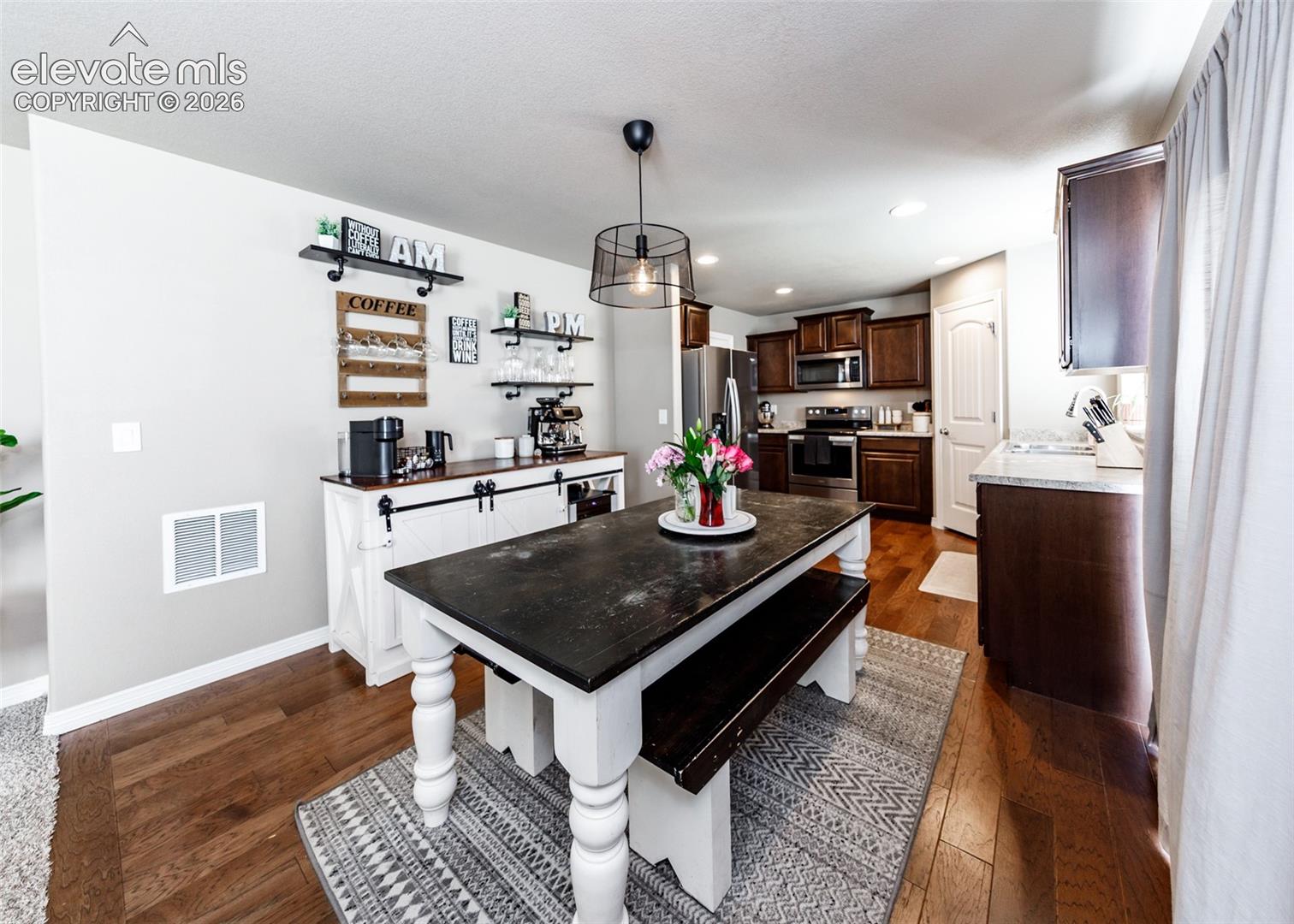 Kitchen featuring dark wood-finish cabinetry, stainless steel appliances, wood-finish flooring, and a suspended drum pendant light fixture
