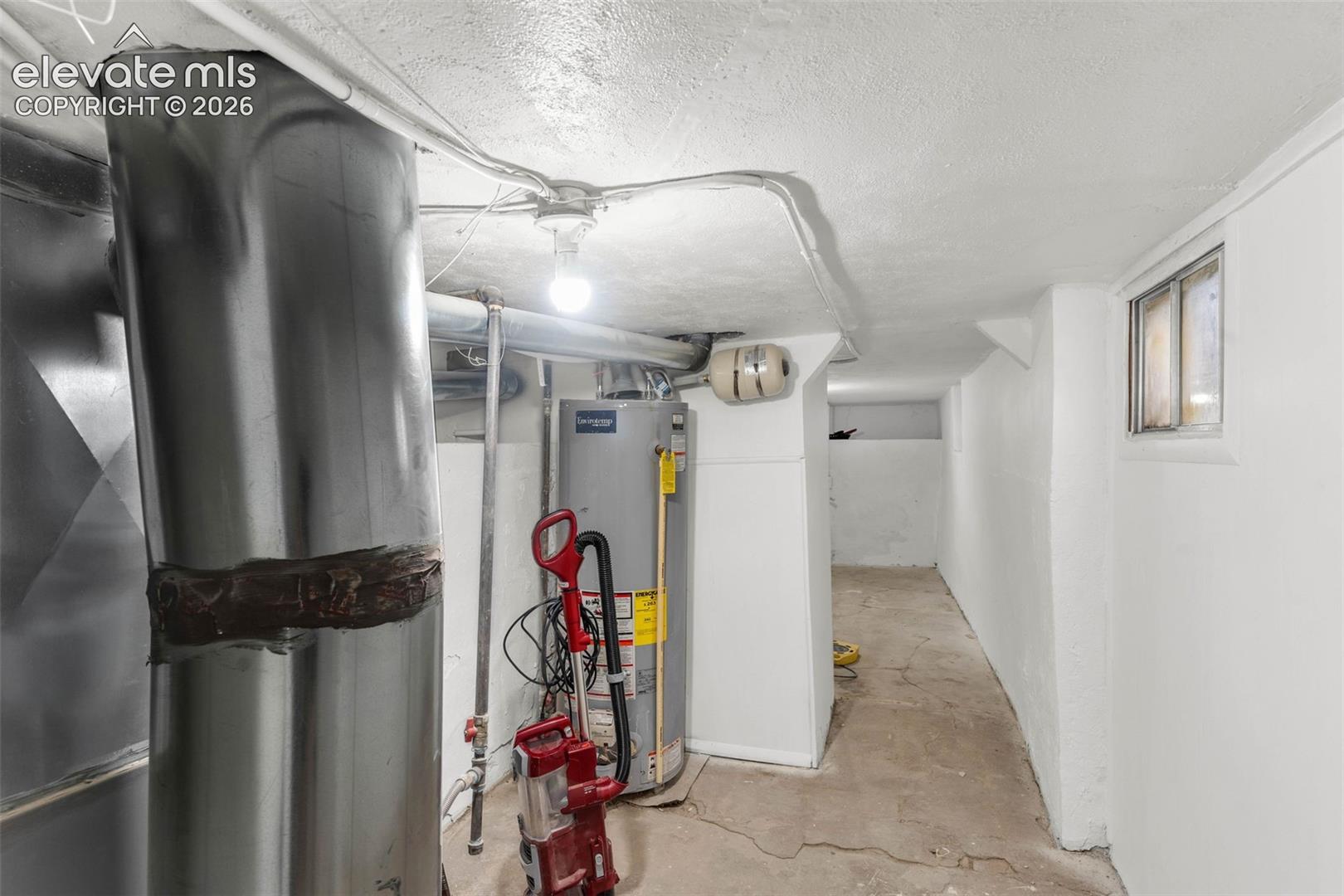 Utility area featuring a concrete floor, painted masonry walls, a gas water heater, and a single-pane window