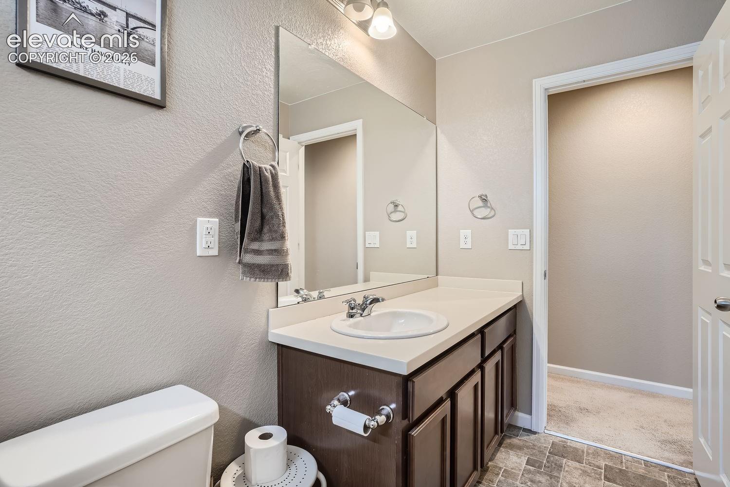 Bathroom featuring a vanity with dark wood-finish cabinetry, a solid-surface countertop, an integrated sink, a large wall-mounted mirror, and tile flooring