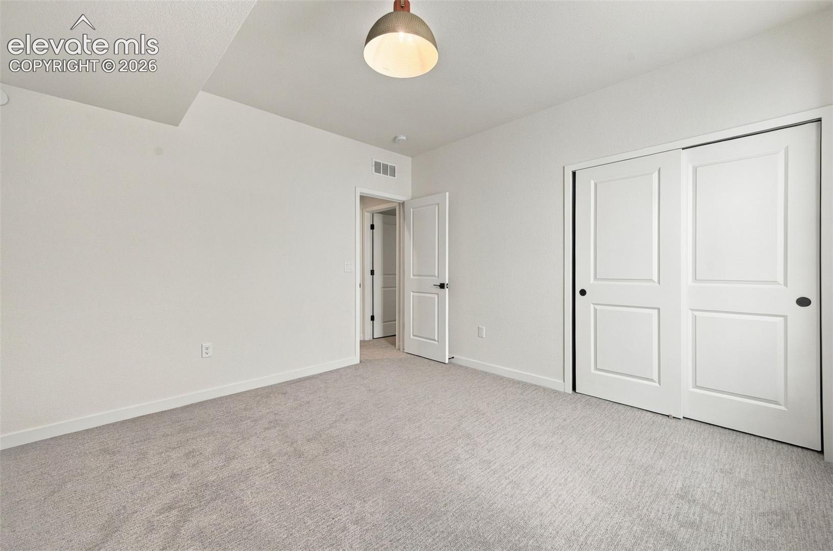 Neutral-toned carpet flooring, sliding double-panel closet doors, and a brushed-metal industrial pendant light fixture