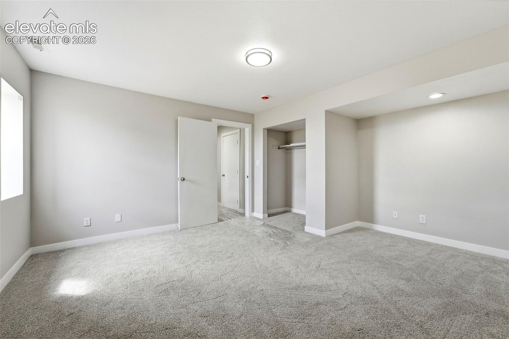 Soft gray wall paint with light gray carpeting, featuring an open closet with a built-in hanging rod, a flush-mount ceiling light, and recessed lighting
