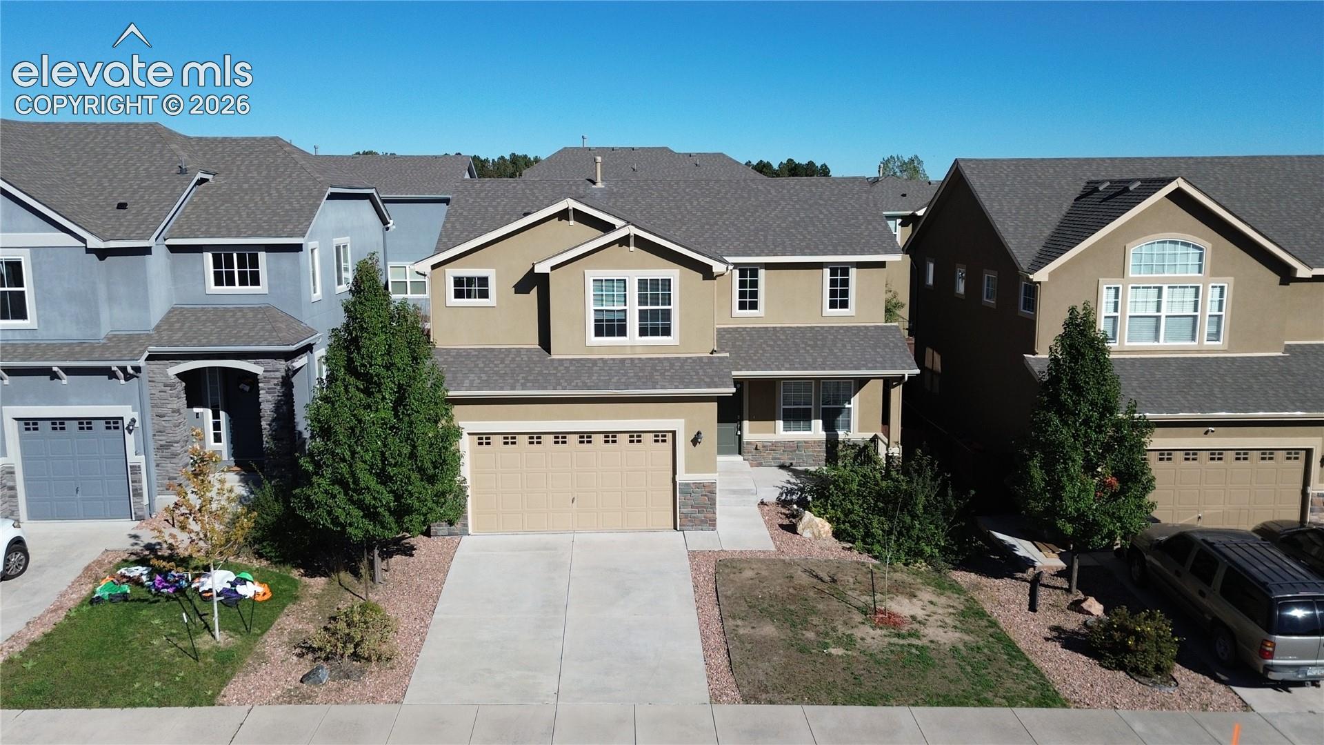 Two-story exterior featuring a neutral stucco facade, stone veneer accents, an attached two-car garage, and a composition shingle roof