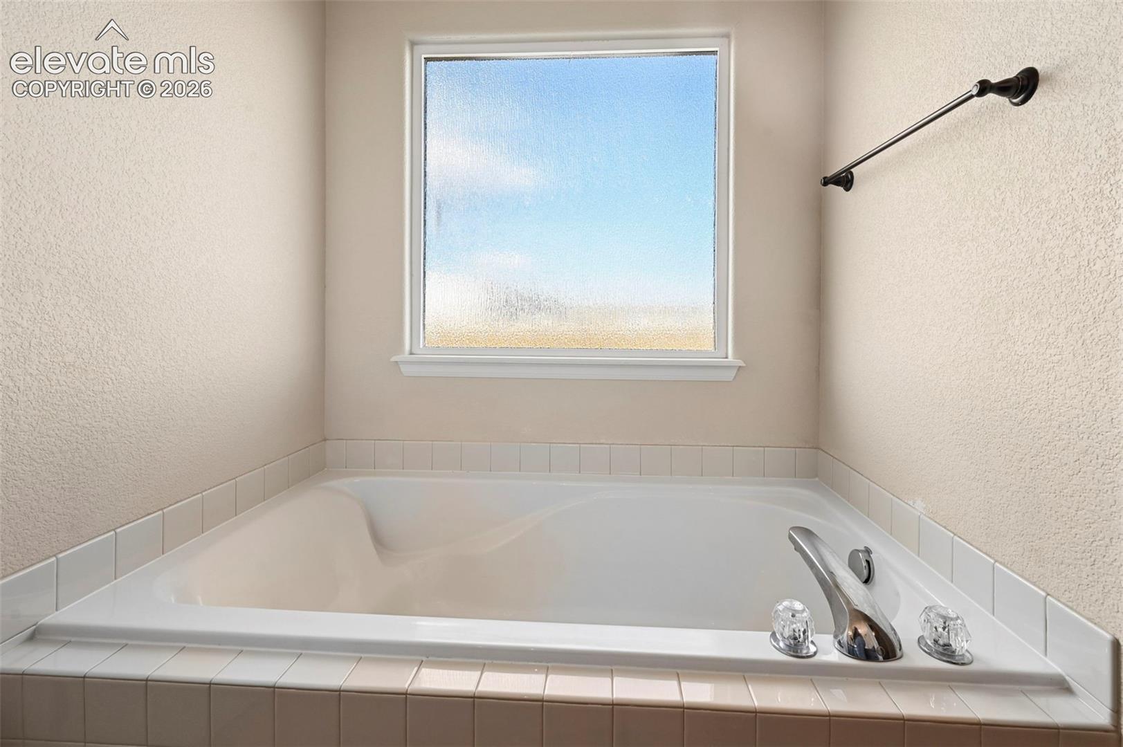 Soaking tub with a tiled surround, frosted glass window, and chrome-finish plumbing fixtures