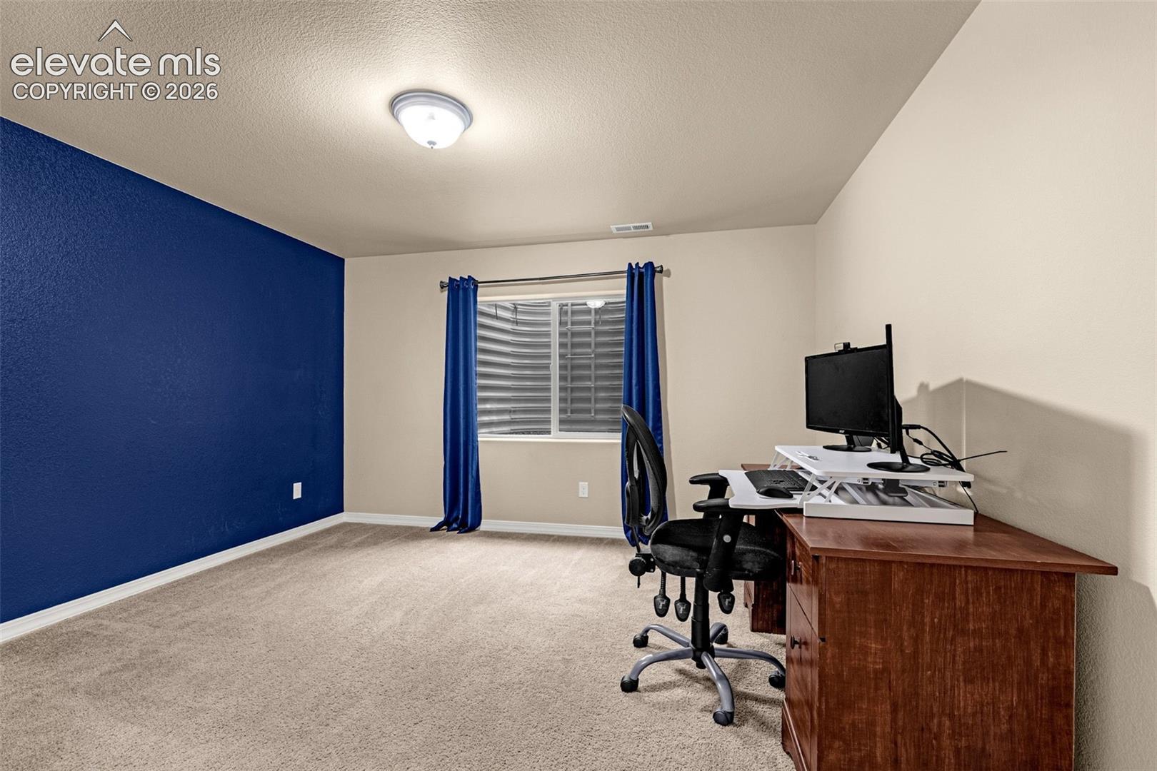 Interior space featuring neutral carpeting, a bold navy accent wall, and a recessed window with a corrugated metal egress well
