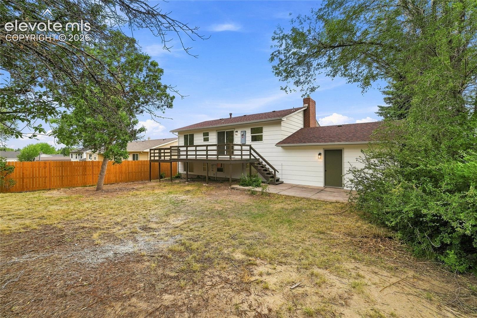 Expansive backyard featuring a raised deck, a privacy fence, and mature trees