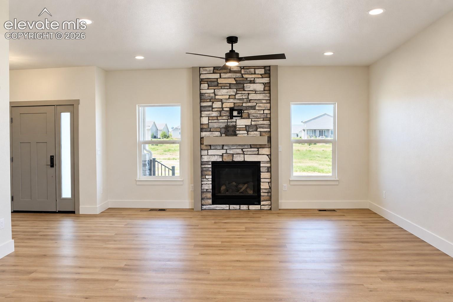 Living area featuring a stone-clad fireplace, wood-finish flooring, recessed lighting, a ceiling fan, and large windows