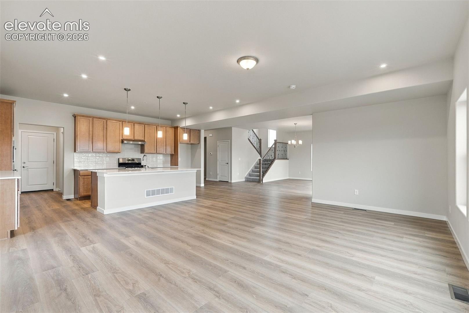 Open-concept interior featuring wood-finish flooring, a central island with pendant lighting, shaker-style cabinetry, and a subway tile backsplash