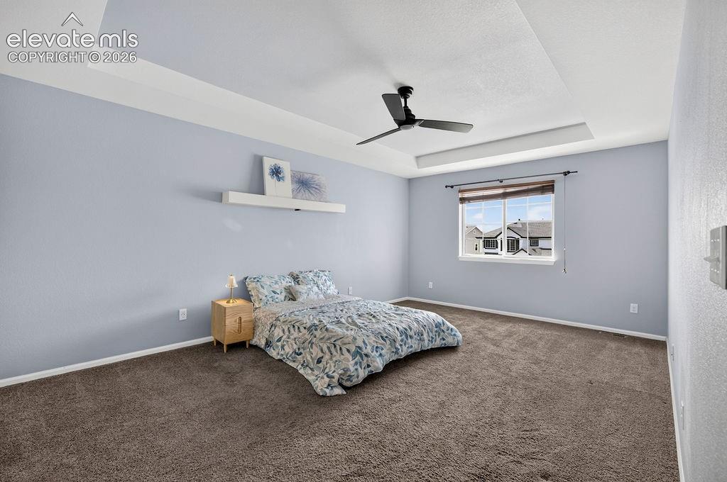 Tray ceiling with recessed lighting, ceiling fan, window with blinds, and wall-to-wall carpeting