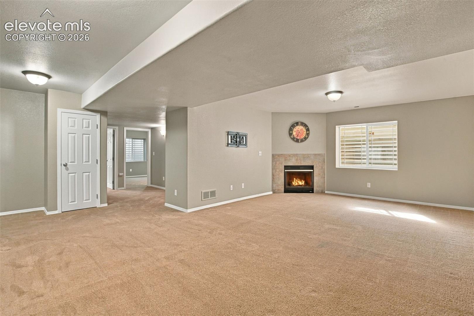 Carpeted room featuring a corner fireplace with a tile surround, a window with horizontal blinds, and a white six-panel door