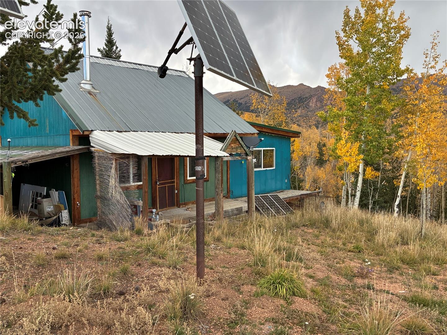 Exterior featuring metal roofing, solar panel array, wood siding, and a covered porch, set against a mountainous backdrop