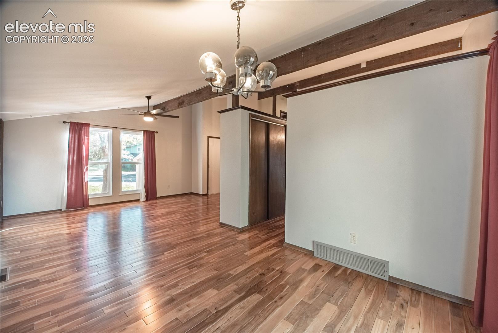 Vaulted ceilings with exposed timber beams, wood-finish flooring, multi-globe chandelier, ceiling fan, and double-door closet with wood-finish trim
