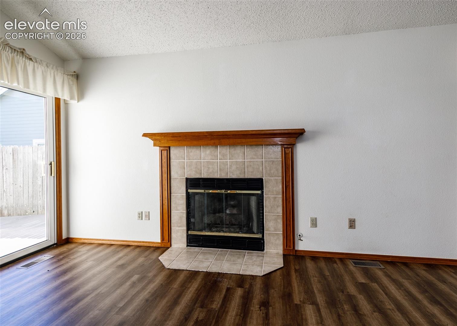 Wood-finish flooring, fireplace with tile surround, wood mantel, and glass sliding door