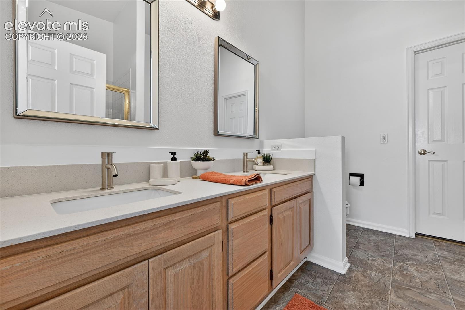 Double vanity featuring a neutral-toned countertop with dual integrated rectangular sinks, light wood-finish cabinetry, framed rectangular mirrors, and metal-finish faucet fixtures