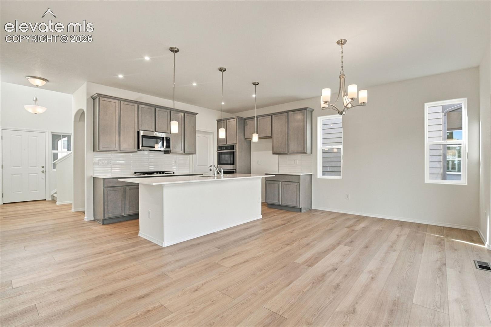 Kitchen featuring grey cabinetry, white countertops, a central island, wood-finish flooring, and multi-light chandelier fixtures