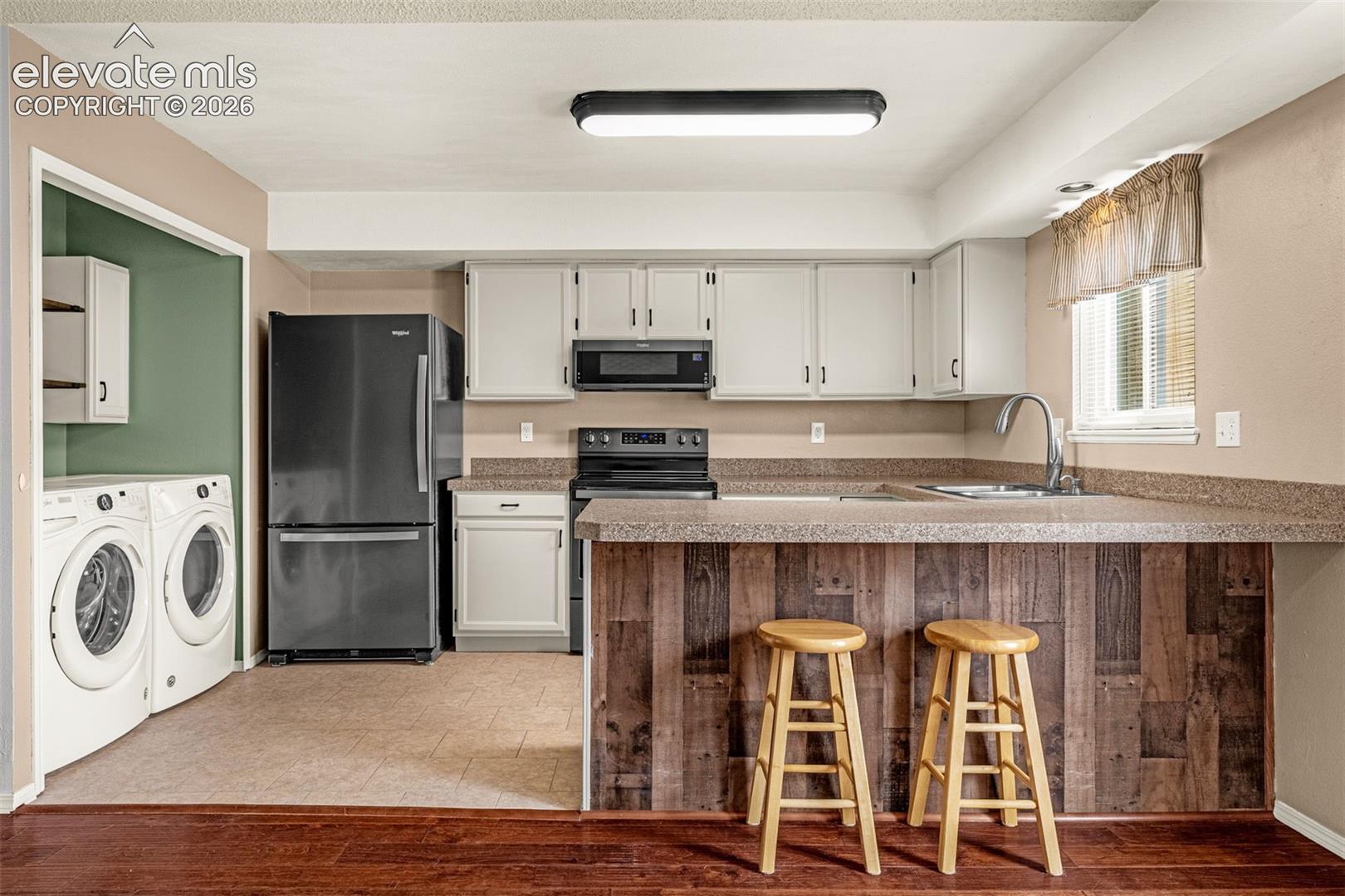 Kitchen with light-colored cabinetry, dark appliances, and a wood-finish breakfast bar