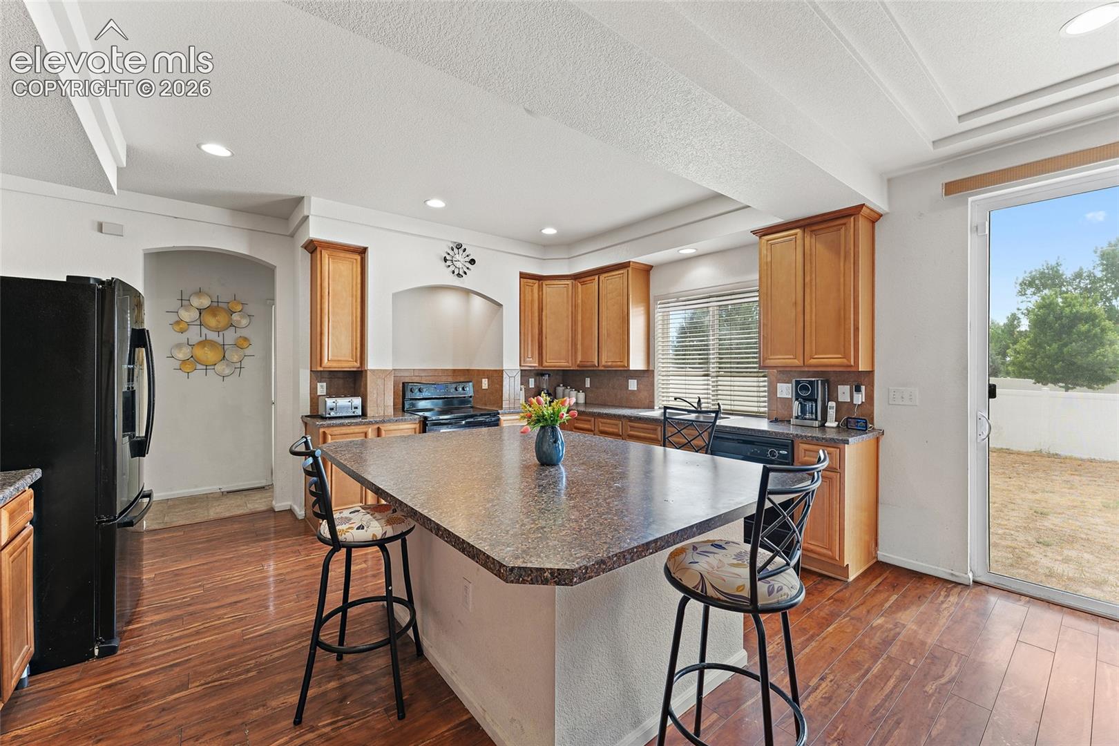 Kitchen featuring wood-finish cabinetry, central island with stone-finish countertop, wood-finish flooring, and sliding glass door