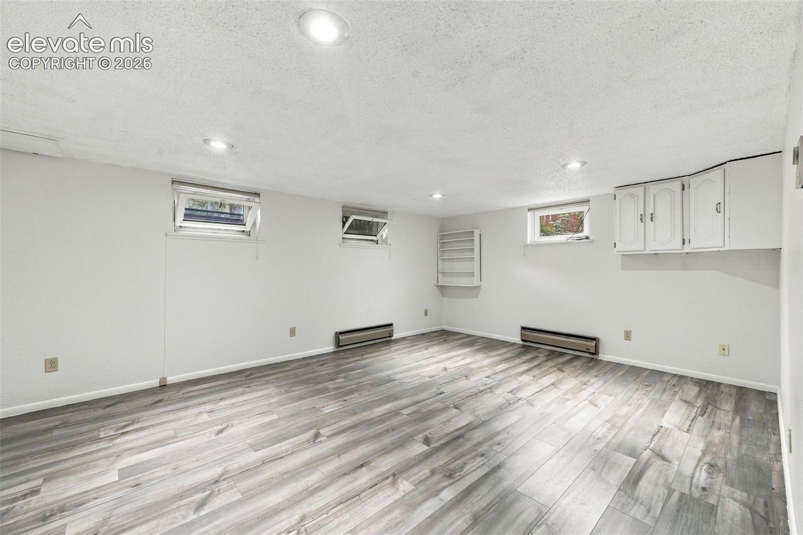 Wood-finish flooring, recessed lighting, three casement windows, wall-mounted cabinetry, and built-in wall shelving