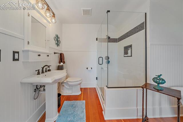 Full bathroom with a stall shower, wainscoting, wood finished floors, and a decorative wall