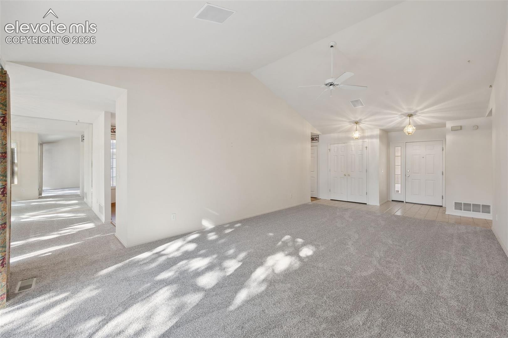 Vaulted ceilings featuring a central paddle fan, dual flush-mount light fixtures, wall-to-wall carpeting, and a multi-panel entry door with a sidelight