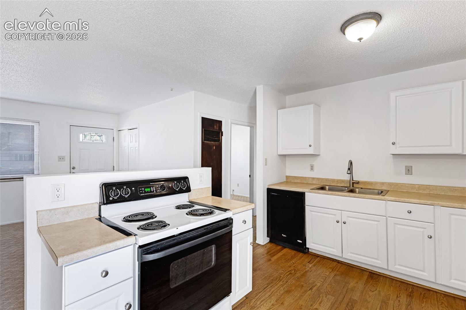 Kitchen featuring white cabinetry, light countertops, wood-finish flooring, a black-and-white range, and a double-basin stainless steel sink with a gooseneck faucet