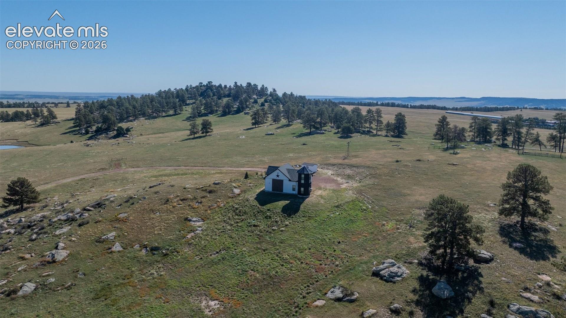 Elevated acreage featuring expansive grasslands, native rock outcroppings, mature evergreen trees, and a detached structure with a dark-tone gabled roof