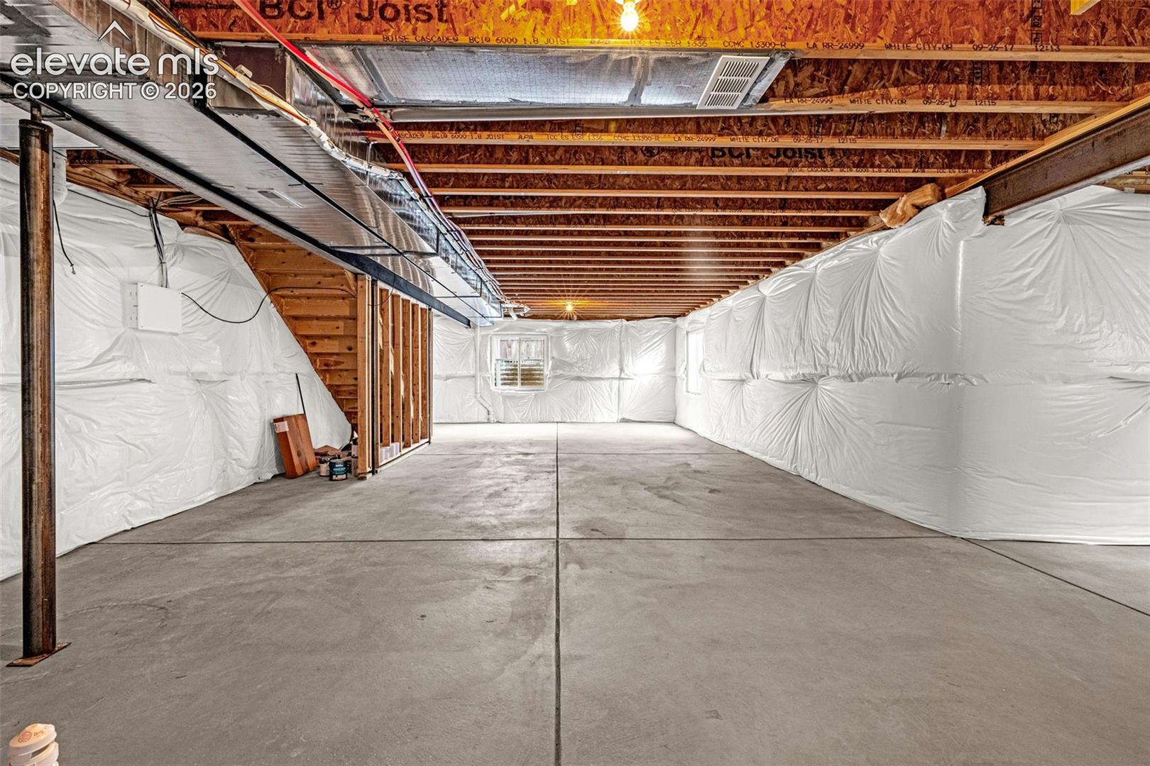 Unfinished basement featuring exposed wood joists, concrete flooring, and a single window