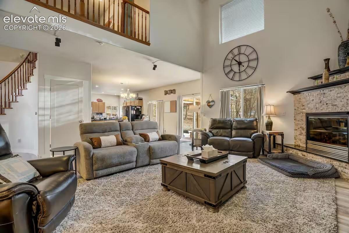 Vaulted living space featuring a stone-clad fireplace, high ceilings, large windows, and a second-story balcony