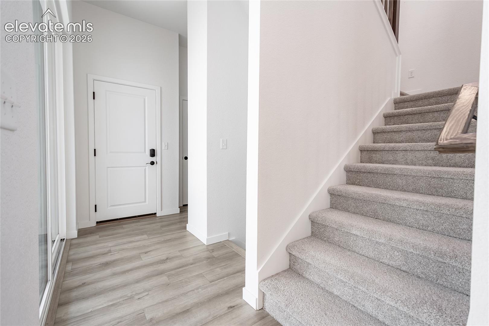 Entryway featuring wood-finish flooring, a neutral color palette, and a carpeted staircase with a wood-finish handrail