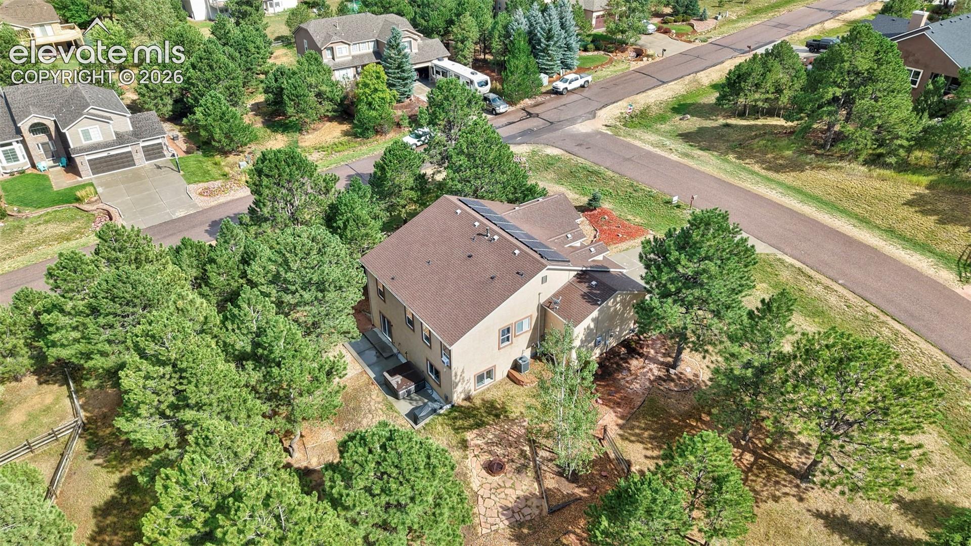 Two-story residence with a brown shingle roof, solar panels, and a surrounding treed landscape