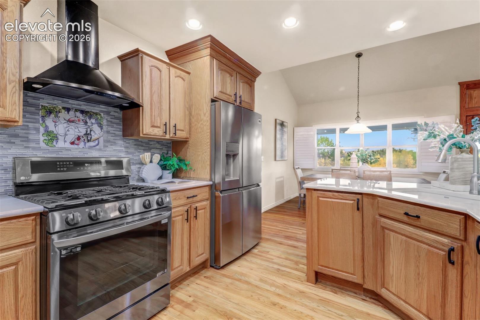 Kitchen featuring wood cabinetry, stainless steel appliances, a multi-tonal tile backsplash, quartz countertops, and wood-finish flooring