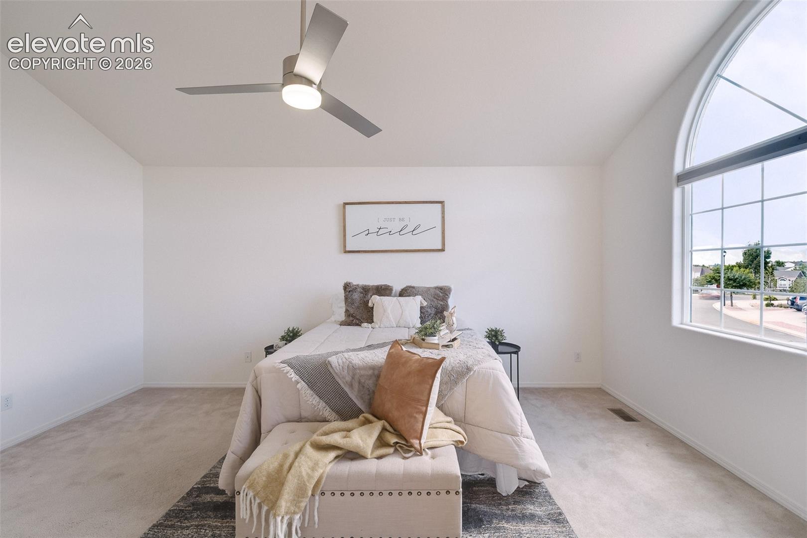 Vaulted ceiling with a contemporary ceiling fan, large arched window, light-toned carpeting, and white wall finishes