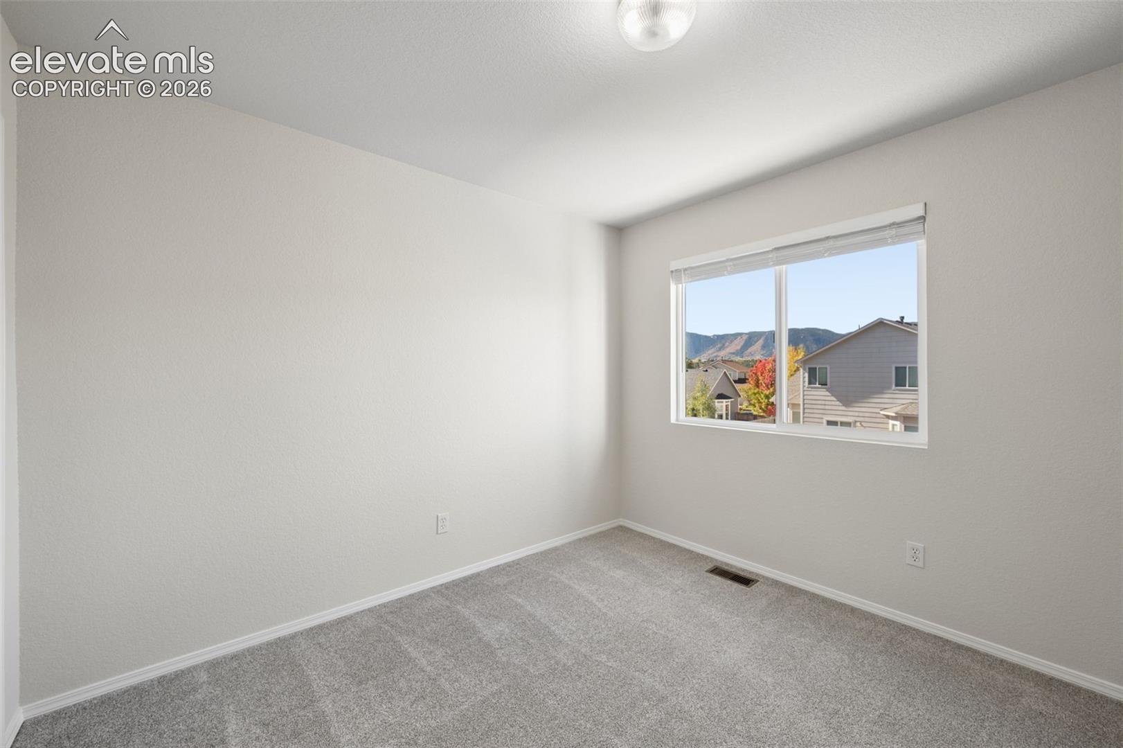 Neutral-toned interior space featuring light-colored wall paint, plush carpeting, a large sliding window, and ceiling-mounted lighting