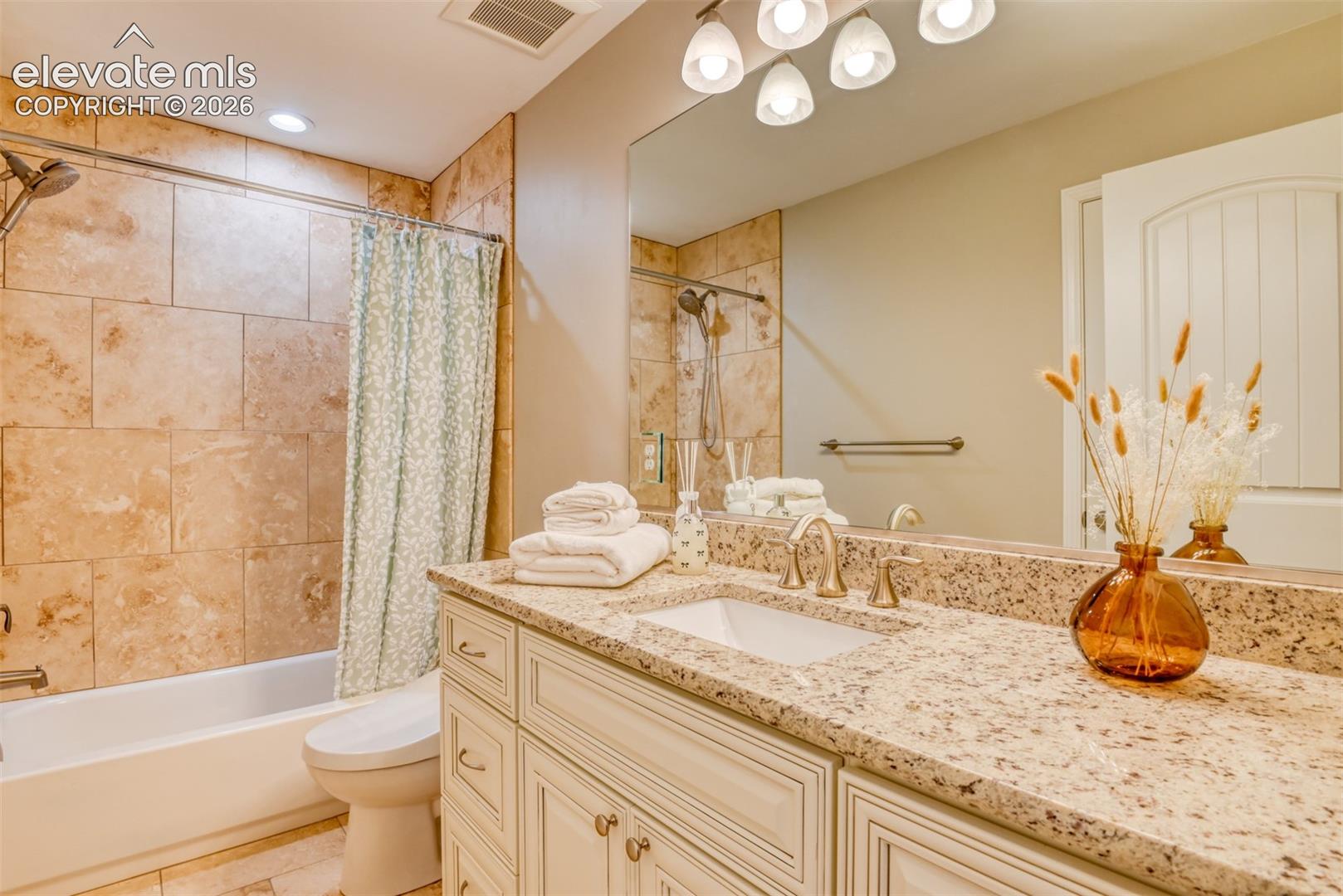 Granite-style countertop with an undermount sink, a vanity with paneled cabinetry, a full-width mirror, a tiled shower surround, and a tub.