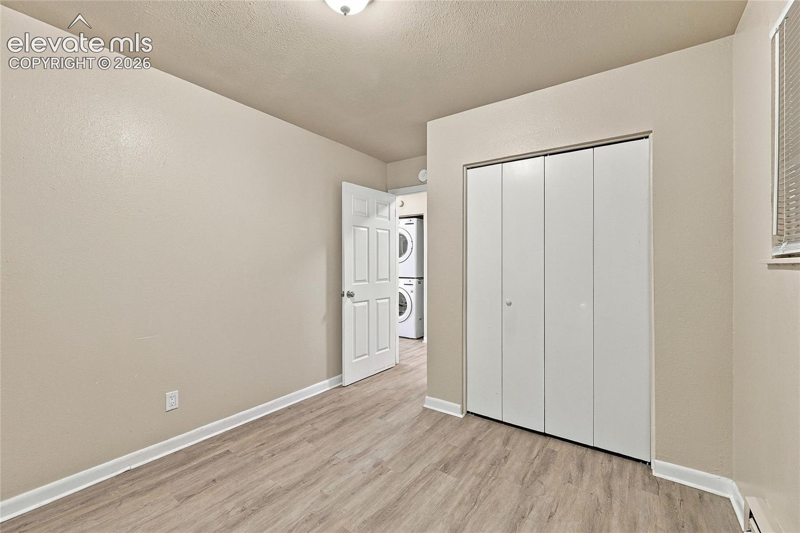 Neutral-toned interior featuring wood-finish flooring, a white six-panel door, and a built-in closet with white bifold doors