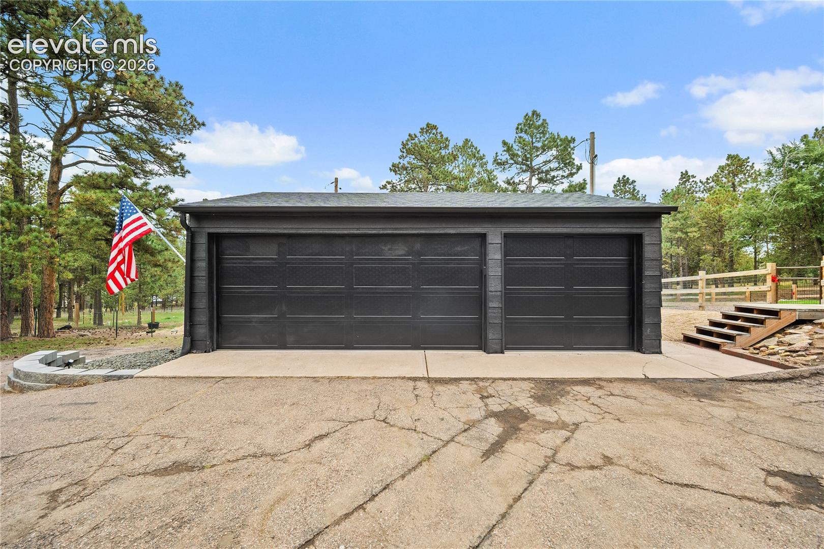 Detached multi-car garage featuring black horizontal-panel doors, dark siding, and a concrete apron with stone retaining wall hardscaping