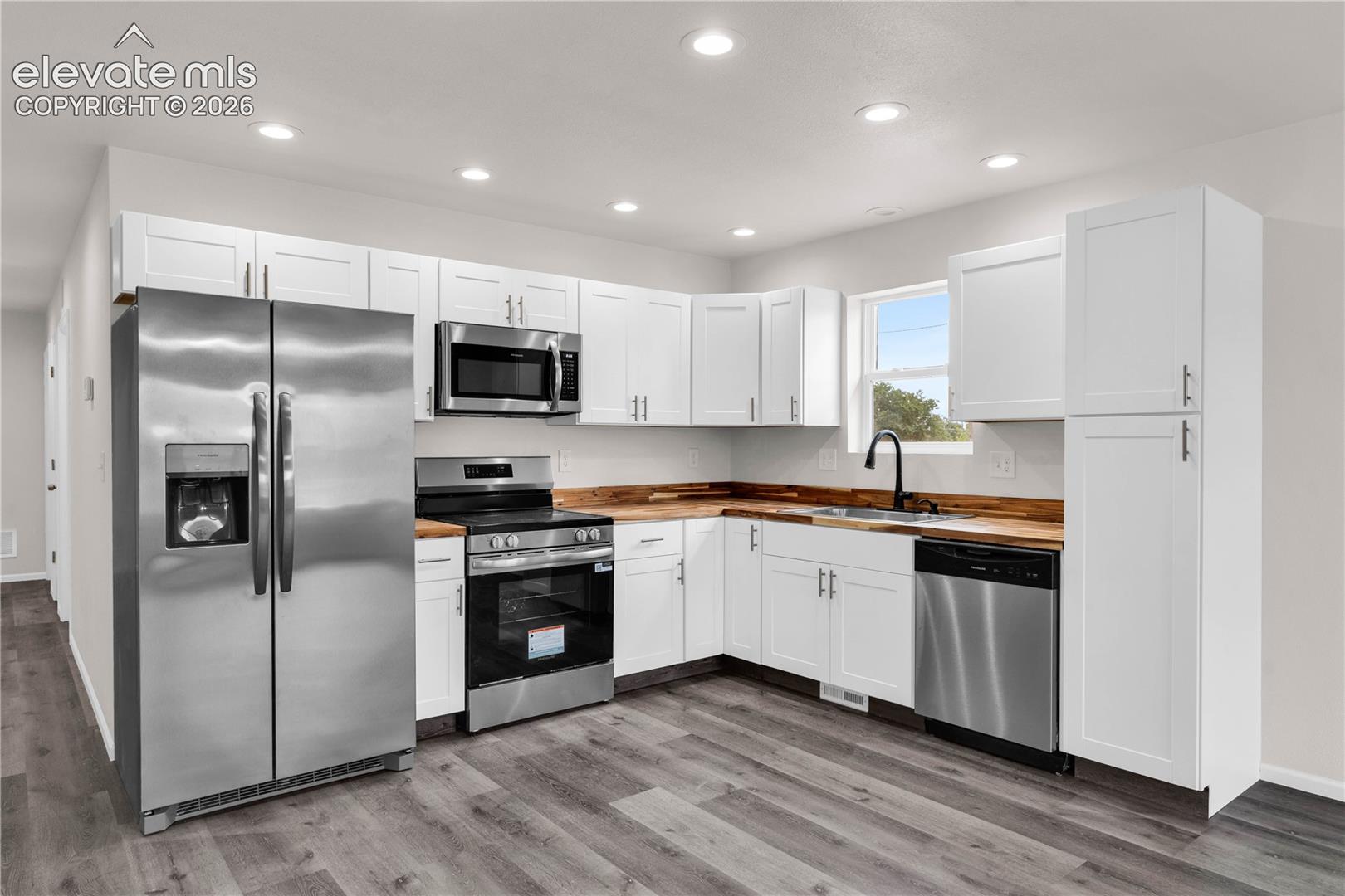 Kitchen featuring shaker-style white cabinetry, wood-finish countertops, stainless steel appliances, matte black faucet, and wood-finish flooring