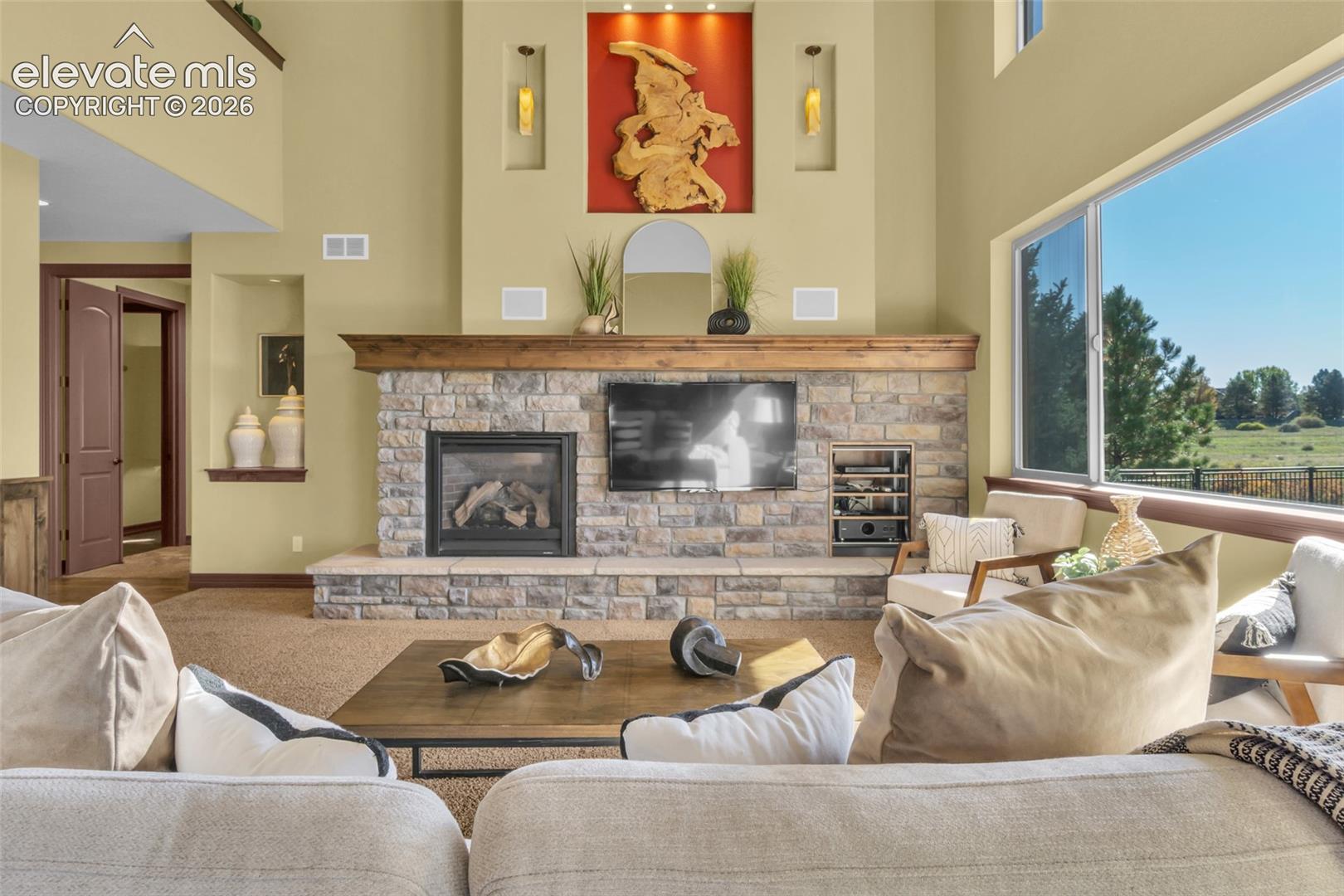 Floor-to-ceiling stone fireplace with a prominent timber mantel, vaulted ceilings, integrated arched wall niches, and expansive horizontal windows