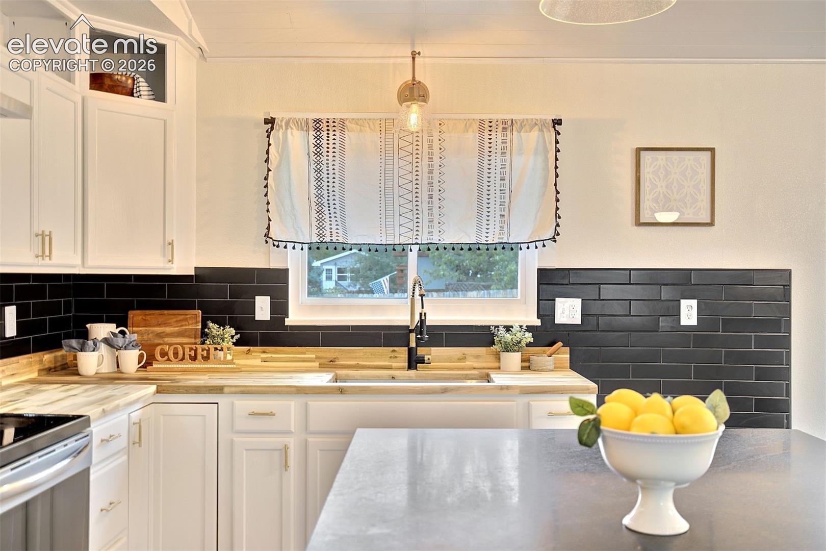 Kitchen featuring white cabinetry with glass-front uppers, wood-finish countertops, matte black subway tile backsplash, farmhouse-style sink, and a high-arc faucet