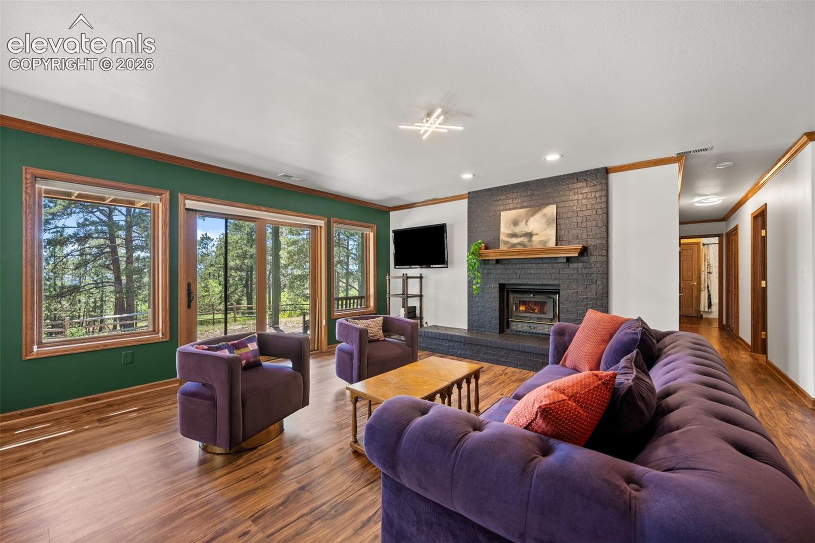 Spacious living area featuring wood-finish flooring, a contemporary fireplace with a black brick surround and wood mantel, expansive windows, and a glass sliding door