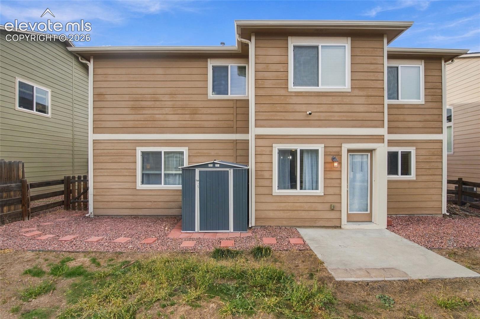 Two-story residence with horizontal siding, a concrete rear patio, integrated metal storage shed, and stone ground cover