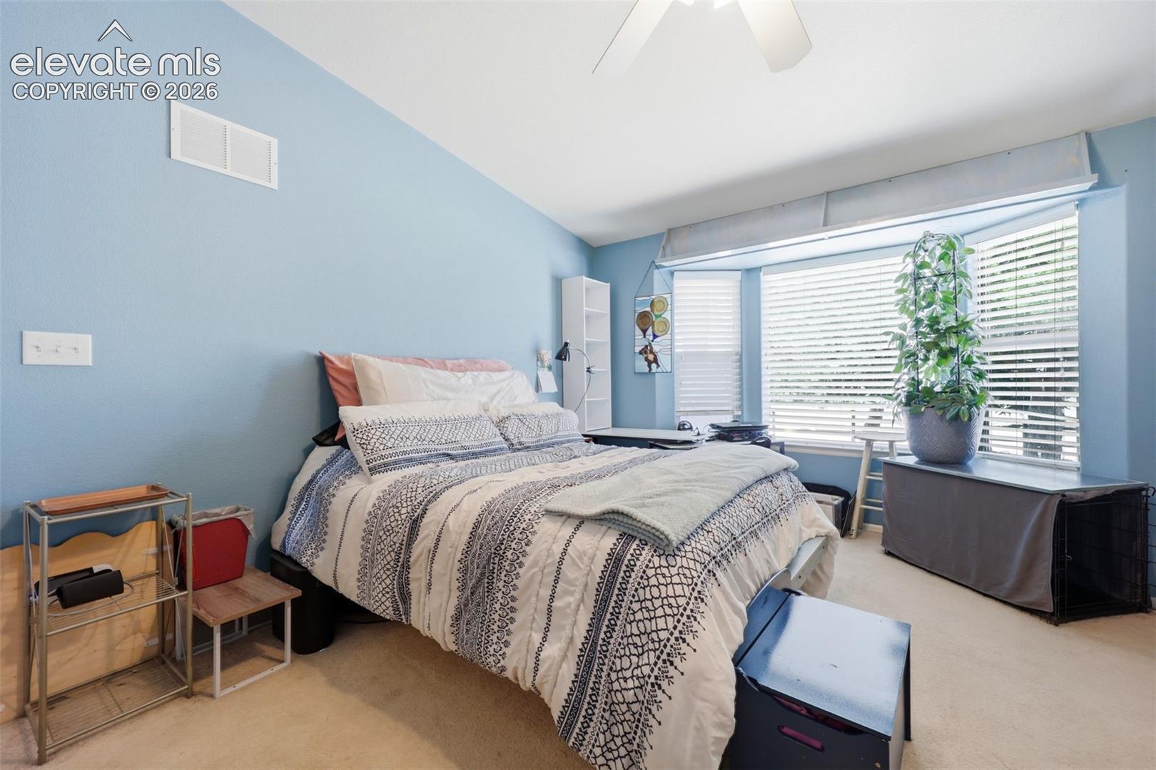 Carpeted room featuring a bay window with horizontal blinds, a sloped ceiling, and a ceiling fan