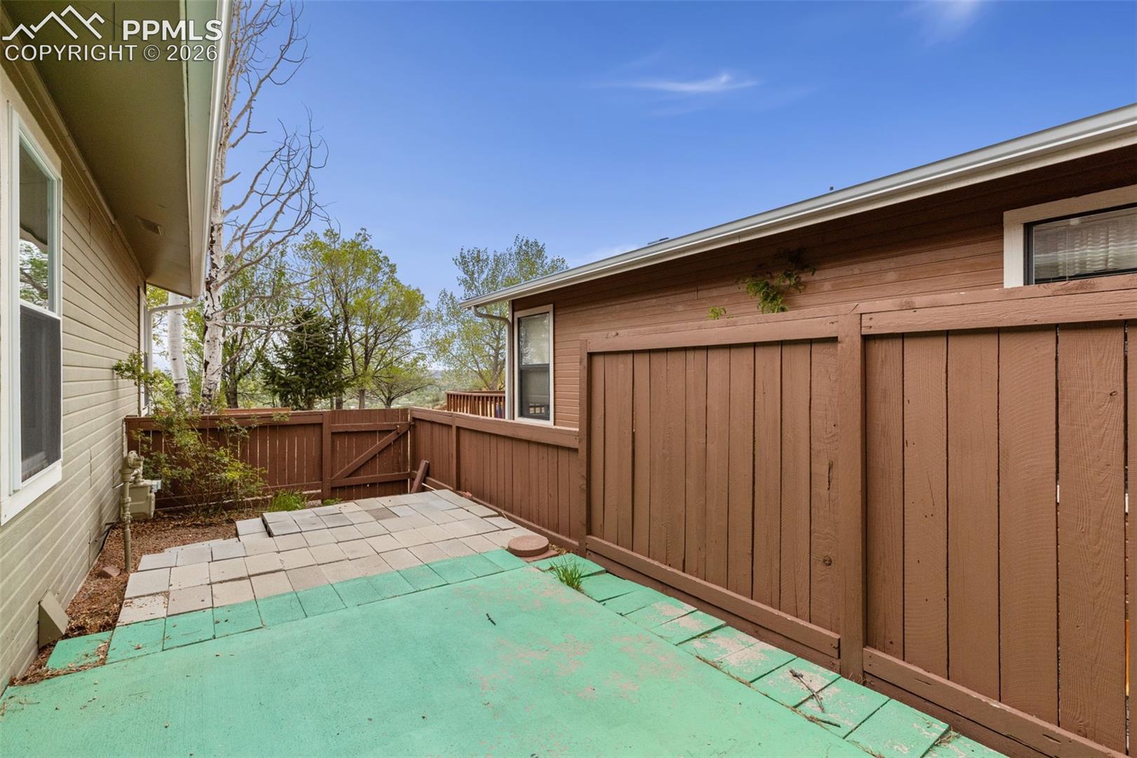 The property features an outdoor patio area with a partial concrete and partial paver surface, enclosed by a brown wooden fence