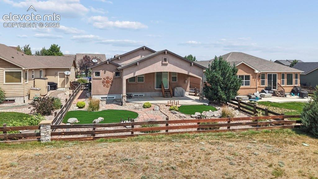 Rear exterior featuring a covered patio, artificial turf, stone patio, and wood fencing with stone columns