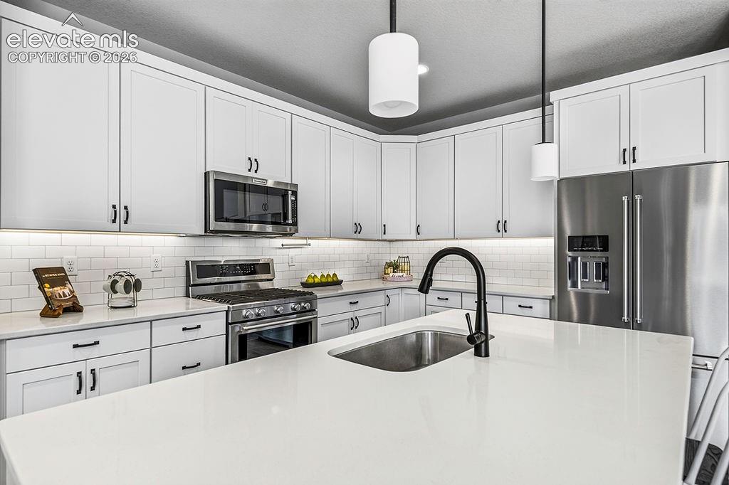 Modern kitchen featuring a large island with an undermount sink and matte black faucet, stainless steel appliances, white shaker cabinetry with dark hardware, subway tile backsplash, and integrated under-cabinet lighting