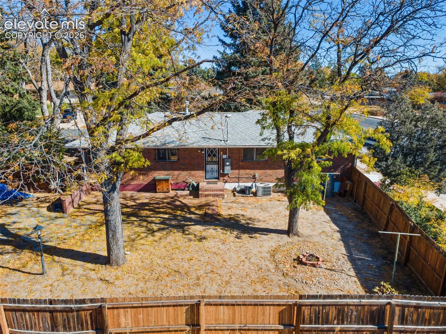 Expansive backyard featuring mature deciduous trees, a privacy fence, and a brick exterior home with a shingle roof